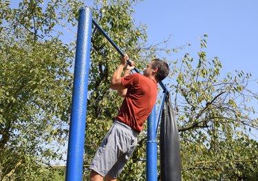 The man pulls himself up on the bar. Playing sports in the fresh air. Homemade Horizontal bar in the backyard.