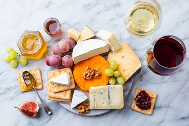 Assortment of cheese, grapes with red and white wine in glasses. Marble background. Top view.