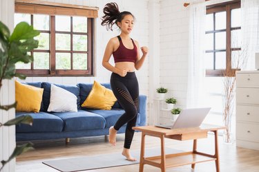 young Asian woman wearing sports bra and leggings working out at home with laptop