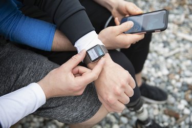 Hands wearing running watch and holding a running app