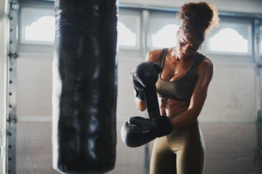 woman covered in sweat from boxing punching bag taking off gloves