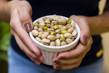 Hand holding white pot with pistachio to get the health benefits of pistachios and pistachio nutrition