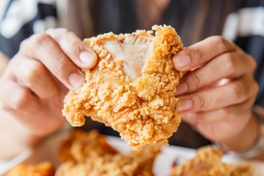 Hand holding Fried chicken and eating in the restaurant because fried eats are food that cause constipation