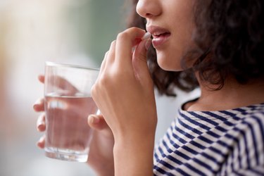 a person taking a pain reliever pill with a glass of water, as a natural remedy for swimmers ear