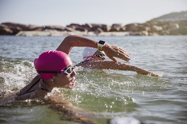 Determined female open water swimmer with smart watch swimming in sunny ocean