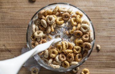 overhead shot of milk being poured into iron-rich cereal on wooden table