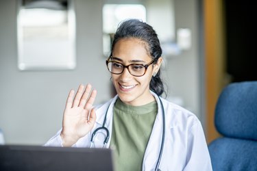smiling doctor waving to patient on laptop during telemedicine appointment