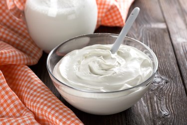 Glass bowl full of sour cream beside cloth on a wooden table