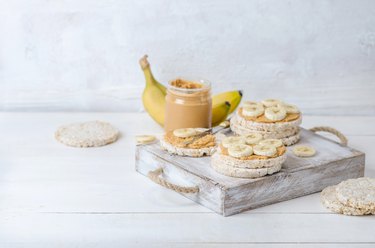 Healthy breakfast with rice cakes with peanut butter and slices of banana on white wooden table. Space for text.