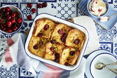 Cherry bread and butter pudding on blue and white table with cherries