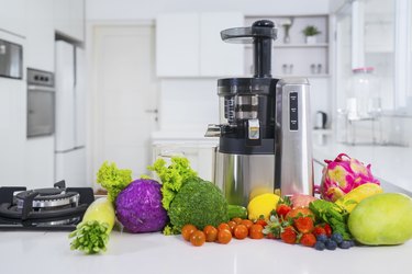 Juicer with various fruits and vegetables in kitchen