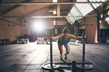 Sportive woman pushing bogie with weight disks