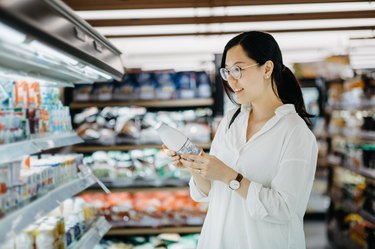Young Asian woman grocery shopping in supermarket and holding a bottle of fresh milk