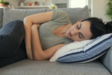 a person lying on the couch holding their stomach because their stomach is making noises