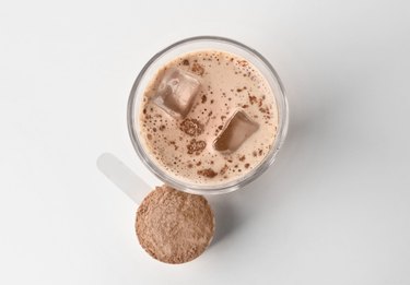 Glass with protein shake and powder in scoop on white background