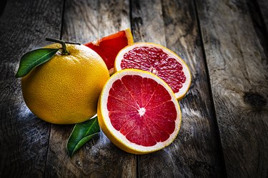 Whole and sliced grape fruit shot on rustic wooden table