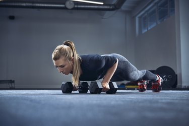 Woman practicing dumbbell push-up exercise at gym