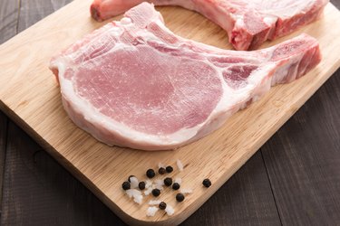 Raw pork chop steak and salt, pepper on wooden background