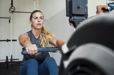 Focused athlete exercising on rowing machine in crossfit gym