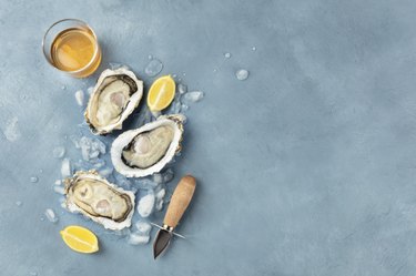 Fresh raw oysters, shot from above on ice with a glass of white wine, lemon slices, shucking knife and copy space