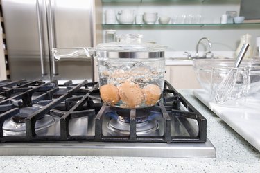 Brown eggs in glass pot of boiling water on stove