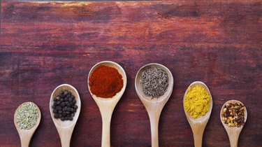 Collage of different spices heaps on wooden background and in wooden spoons