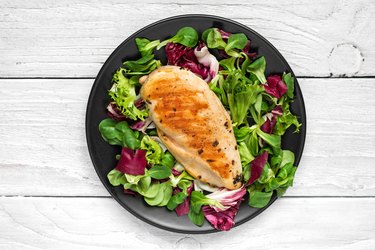 grilled chicken breast with mixed salad on a black plate with knife and fork