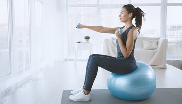 Young woman with gym ball and dumbbells at home, blank space