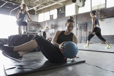 Focused, strong woman doing seated medicine ball twist in gritty gym