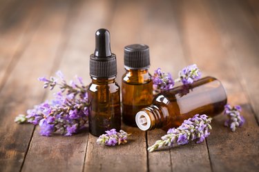 Three bottles of lavender essential oil with dried lavender on a wooden table