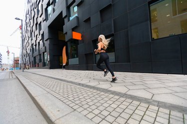 Back view of a fast running fit woman in modern city environment