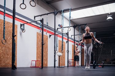 Young woman training, skipping in gym, full length