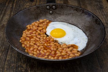 Fried egg and baked beans in frying pan on wood