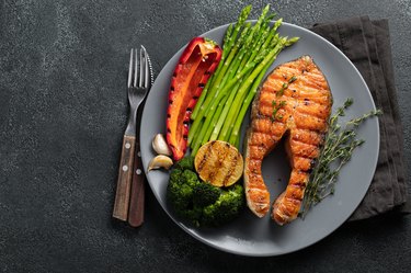 Tasty and healthy salmon steak with asparagus, broccoli and red pepper on a gray plate. Diet food on a dark background with copy space. Top view. Flat lay