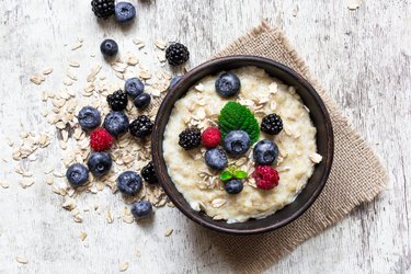 A high fiber-food, oatmeal is served with ripe berries in a bowl on a wooden table