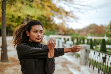 Beautiful young woman doing stretching exercises while standing outdoors.