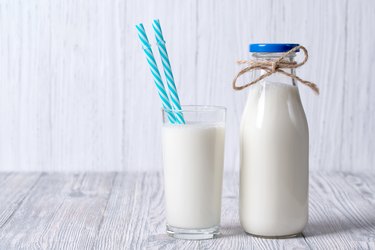Bottle and glass of milk with straws, wooden background