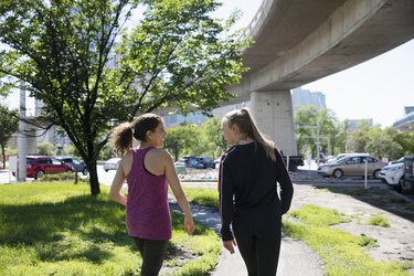 Women talking and walking on sunny, urban path