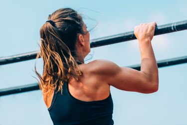 Woman pull-ups herself up on bar on sports ground in park Stock