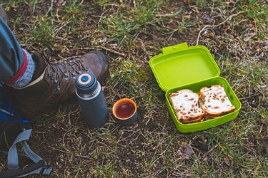 Shoe of hiker with thermos and lunch box in grass. Top view.