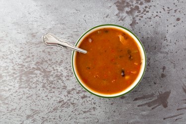 Top view of a bowl of chicken tortilla soup with a spoon on a gray background.