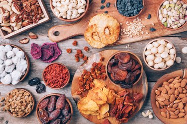 Mix of dried fruits and nuts -brazil nuts, cashew, pecan, almonds, macadamia, pine nuts, hazelnuts, pineapple, raisins, dates, dried apricots, goji, papaya, figs, mulberry on wooden background.Top view. Superfood, vegan, vegetarian concept