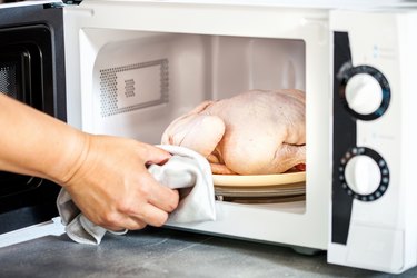 Hand placing raw chicken in the microwave