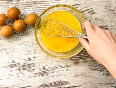 A large glass bowl with a process of beating eggs for cooking.