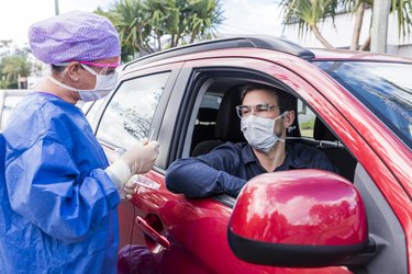A doctor taking a nasal swab from a driver in a red car