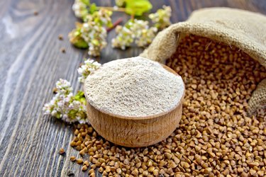 Flour buckwheat in bowl with cereals and flower on board