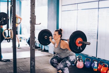 Person squatting with a barbell, demonstrating everything you need to know about squat machines at the gym