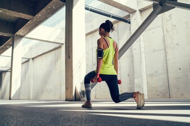 woman doing lunges with dumbbells outside for benefits of full-body workout