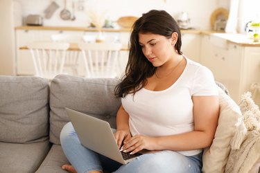 A woman sitting on the couch with her laptop to access a weight-loss forum