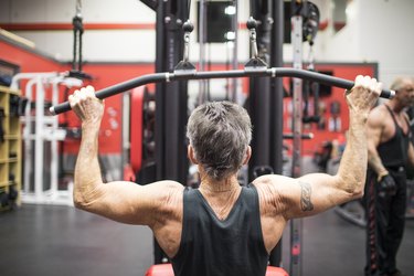 Rear view of elderly man doing Lat Pull Down exercise on gym equipment